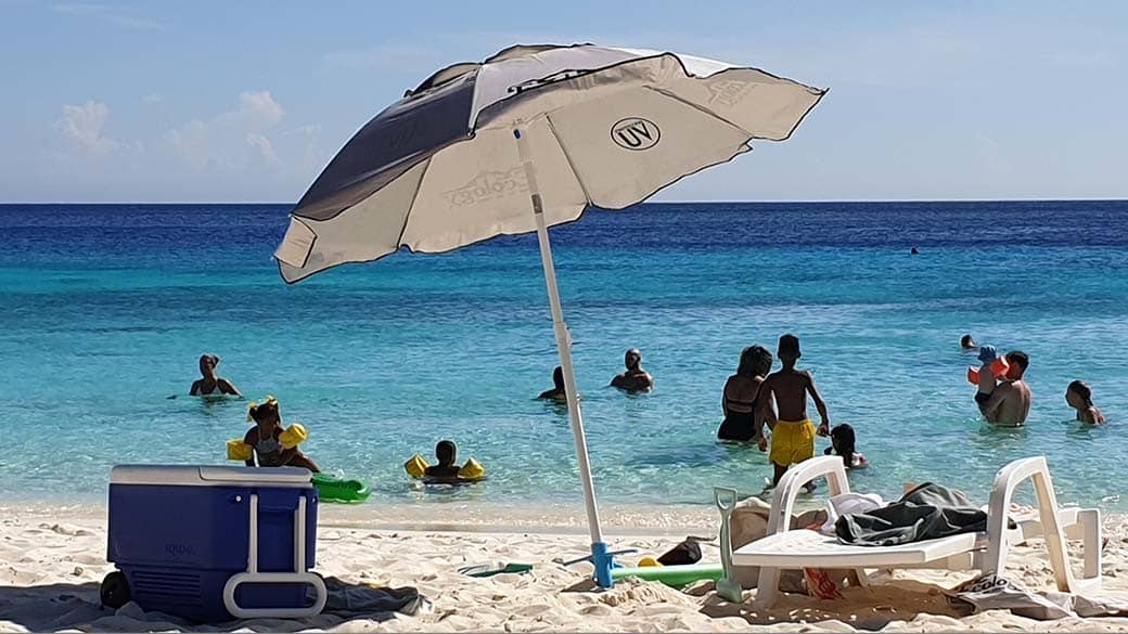 Hauptsache im Schatten: Kühlbox-Trolley unter einem Sonnenschirm vor türkisem Meer